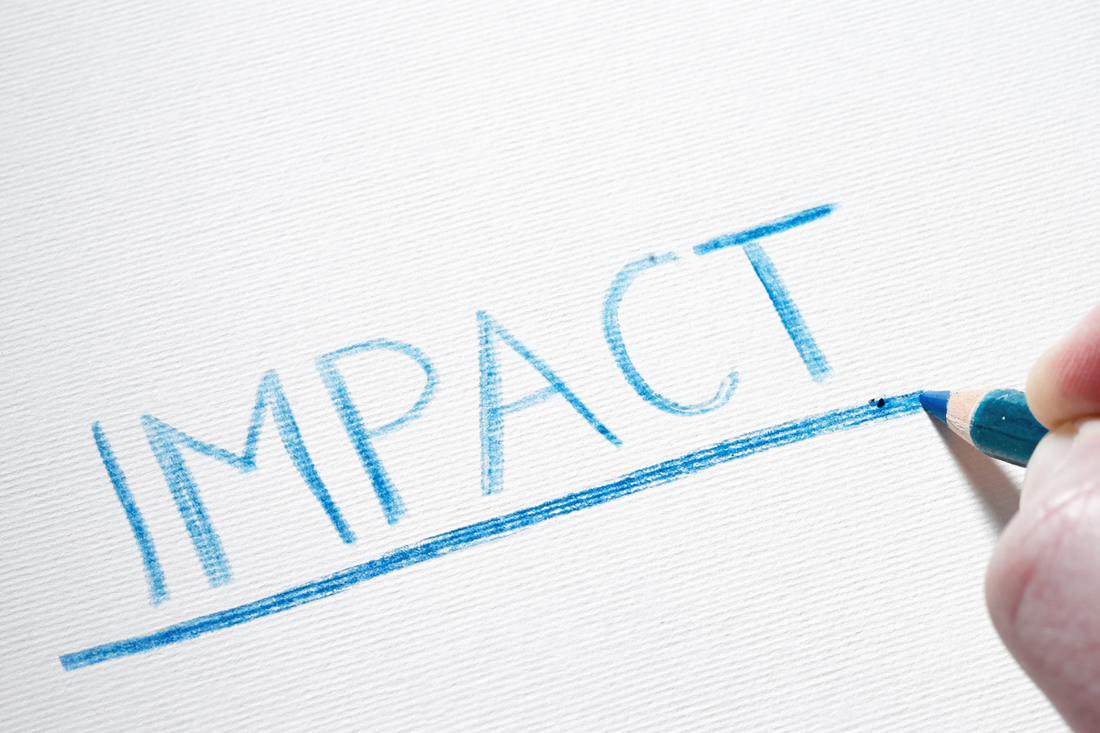 Hand mit einem blauen Bleistift in der Hand, die das Wort "impact" schreibt