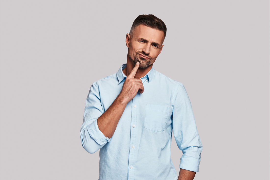 Foto eines Mannes in einem blauen Hemd, der sich an sein Kinn fasst und nachdenklich oder besorgt aussieht, während er über die Folgen der Selbstmedikation mit Alkohol nachdenkt.