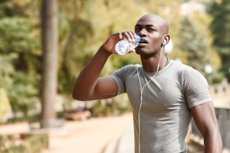 Homme buvant de l'eau en faisant de l'exercice à l'extérieur, illustrant l'importance de l'hydratation à base d'electrolytes pour la santé et la peau
