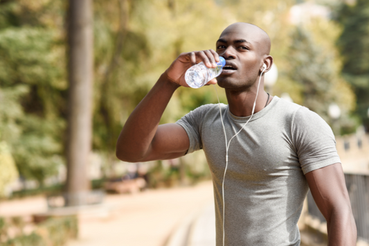Homme buvant de l'eau en faisant de l'exercice à l'extérieur, illustrant l'importance de l'hydratation à base d'electrolytes pour la santé et la peau