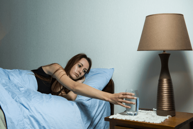 femme venant de se reveiller qui prend un verre d'eau poser sur sa table de chevet