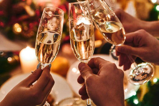 People toasting with champagne flutes against a blurred background of Christmas decorations, exuding a warm, celebratory atmosphere.