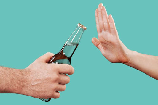 Main refusant poliment une bouteille de bière tendue, sur un fond turquoise uni, symbolisant le choix de ne pas boire d'alcool ou de la sobriété.