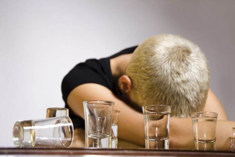 Personne avec se reposant sur ses bras croisés sur une table, entourée de verres à shot vides, dans un état d'épuisement ou d'intoxication.
