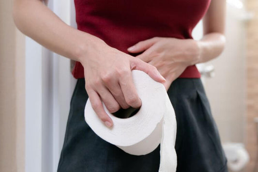 a person standing in a bathroom, holding a roll of toilet paper in their right hand.