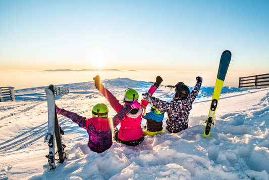 Famille de dos levant les bras au ciel assis sur la neige et admirant les pistes de ski