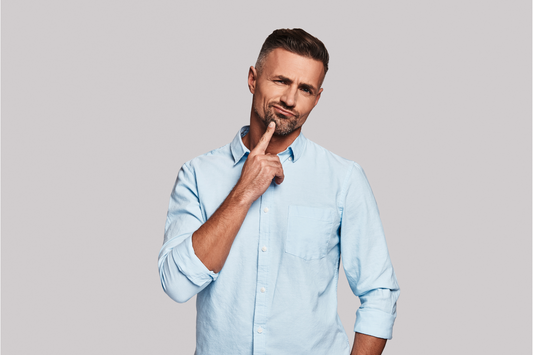 Photo d'un homme en chemise bleue se touchant le menton, l'air pensif ou préoccupé,en train de réfléchir aux conséquences de l'automédication avec de l'alcool.