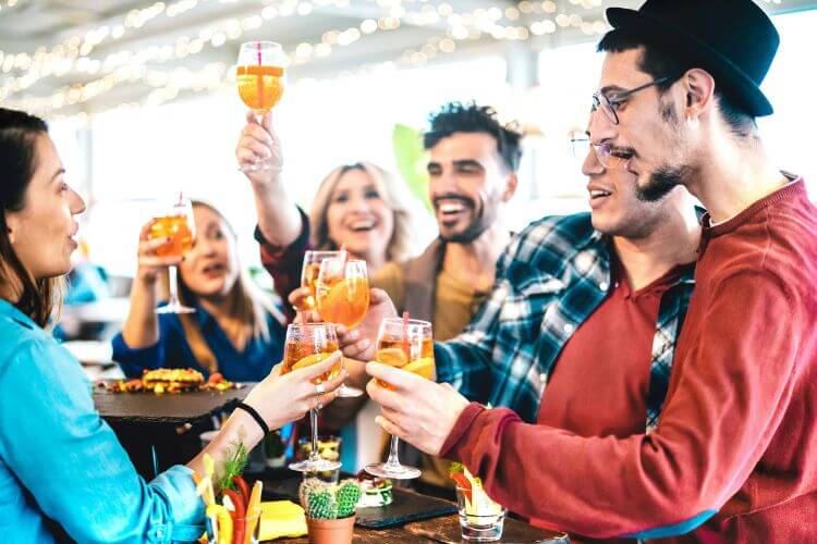 A group of friends toasting with drinks, enjoying their time without worry thanks to HANG-OVER, the solution for hangovers, highlighting a cheerful social gathering.