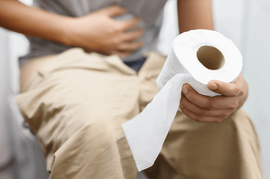 Une personne assise sur des toilettes, souffrant de maux de ventre tenant un rouleau de papier toilette.