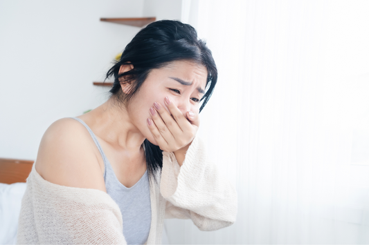 Une femme se tenant l'estomac et l'air souffrant, ce qui pourrait représenter les effets de la nausée après consommation d'alcool ou un symptôme de la gueule de bois.