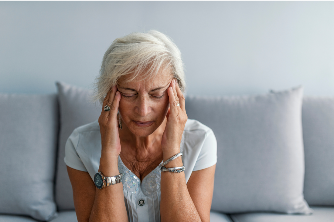 Une femme âgée se tenant la tête, exprimant de la douleur ou du malaise, souvent associée à un mal de tête dû à une gueule de bois.