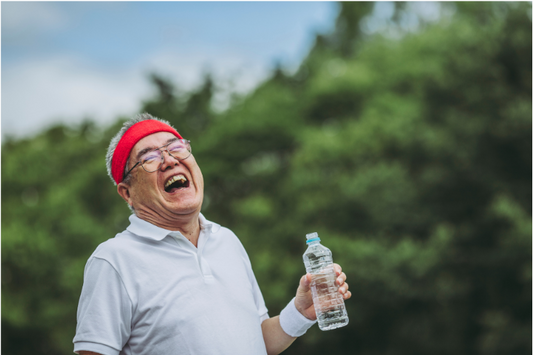 Homme senior souriant en tenue de sport, tenant une bouteille d'eau à l'extérieur. L'image montre l'importance de l'hydratation et de la joie de rester actif et en bonne santé à tout âge.